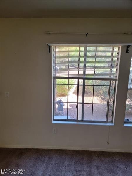 empty room featuring dark colored carpet and baseboards