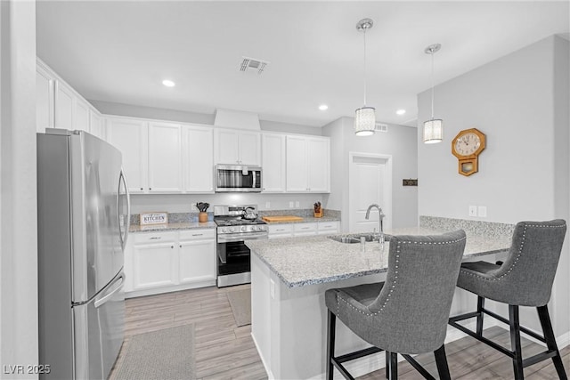 kitchen featuring light stone counters, visible vents, appliances with stainless steel finishes, a peninsula, and a kitchen breakfast bar