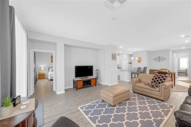 living area with baseboards, light wood-type flooring, visible vents, and recessed lighting