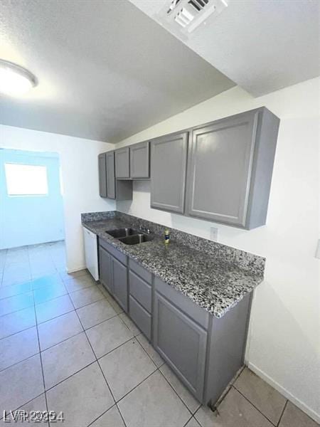 kitchen featuring light tile patterned floors, visible vents, gray cabinetry, white dishwasher, and a sink