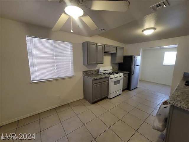 kitchen with light tile patterned floors, white gas range, gray cabinetry, a ceiling fan, and freestanding refrigerator