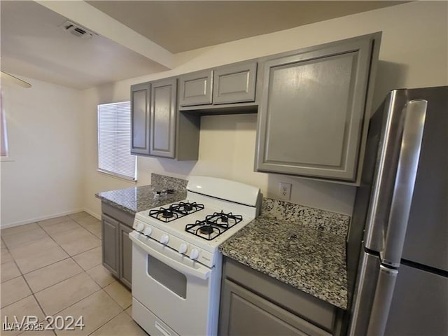 kitchen featuring visible vents, gas range gas stove, freestanding refrigerator, and gray cabinetry