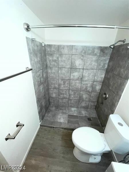 bathroom featuring toilet, tiled shower, and wood finished floors