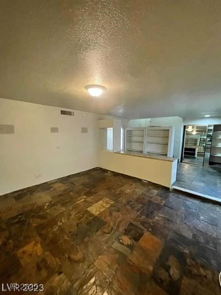 unfurnished living room featuring stone finish flooring, visible vents, and a textured ceiling