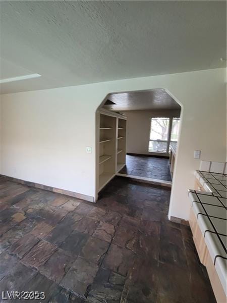 interior space with baseboards, arched walkways, and a textured ceiling