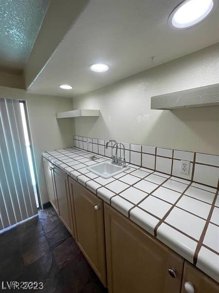 kitchen with tile counters, stone finish floor, open shelves, a sink, and recessed lighting