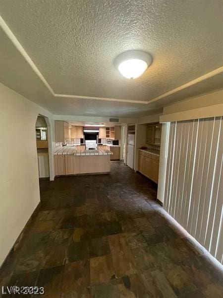 hallway featuring arched walkways, a raised ceiling, a textured ceiling, and dark wood finished floors