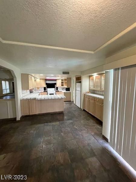 kitchen featuring arched walkways, tile countertops, freestanding refrigerator, a peninsula, and a textured ceiling