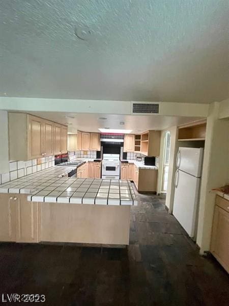 kitchen with a peninsula, visible vents, tile counters, freestanding refrigerator, and open shelves