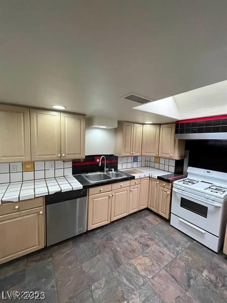 kitchen featuring stainless steel dishwasher, white gas range oven, a sink, and tile counters