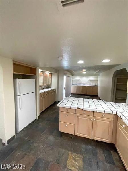 kitchen featuring tile counters, recessed lighting, visible vents, light brown cabinetry, and freestanding refrigerator