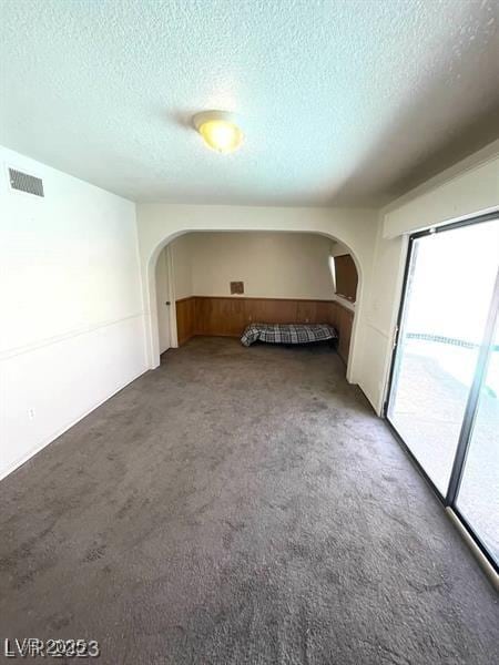 empty room featuring carpet floors, arched walkways, visible vents, wainscoting, and a textured ceiling