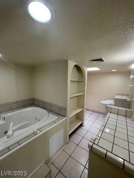 full bath with a textured ceiling, a jetted tub, tile patterned flooring, and visible vents