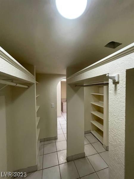 spacious closet featuring arched walkways and light tile patterned flooring