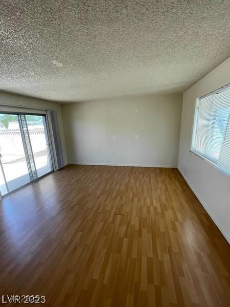 unfurnished room featuring a textured ceiling, baseboards, and wood finished floors