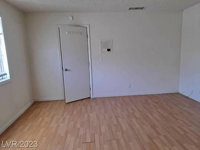 spare room with light wood-style flooring, visible vents, baseboards, and a textured ceiling