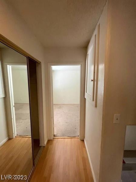 hallway with baseboards, light colored carpet, and light wood-style floors