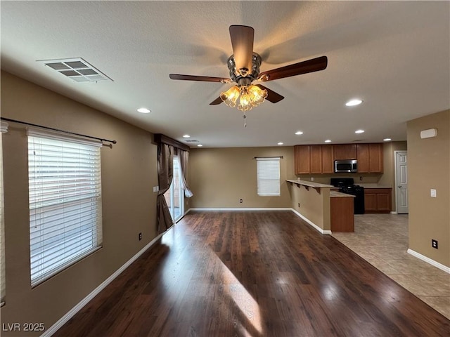 kitchen featuring black gas range, visible vents, stainless steel microwave, open floor plan, and light countertops