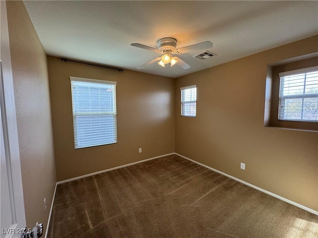 spare room featuring a ceiling fan, dark colored carpet, visible vents, and baseboards