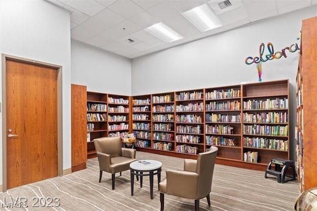 living area featuring a drop ceiling, wall of books, and visible vents