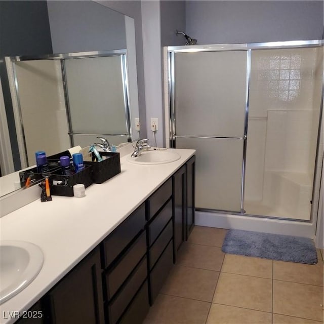 full bath with a stall shower, double vanity, a sink, and tile patterned floors