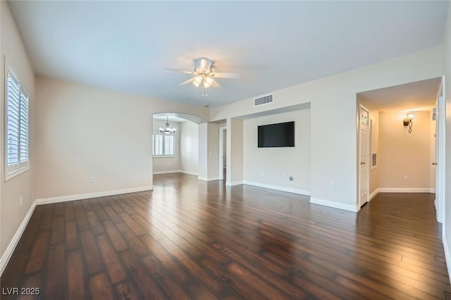 unfurnished living room featuring visible vents, baseboards, dark wood finished floors, ceiling fan with notable chandelier, and arched walkways