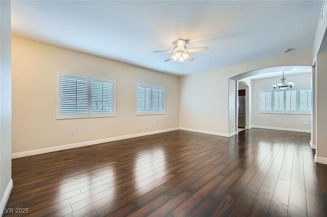 spare room with dark wood-type flooring, ceiling fan with notable chandelier, arched walkways, and baseboards