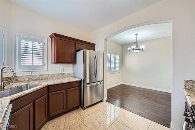 kitchen with light stone counters, an inviting chandelier, arched walkways, freestanding refrigerator, and a sink