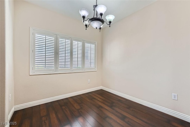 spare room featuring an inviting chandelier, dark wood-style floors, and baseboards