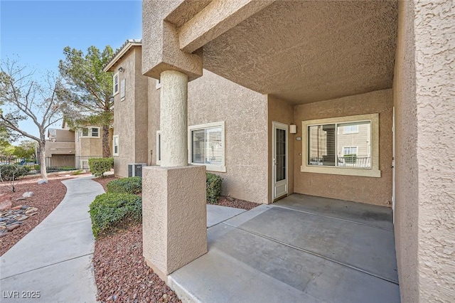 view of exterior entry featuring a patio area, stucco siding, and central AC