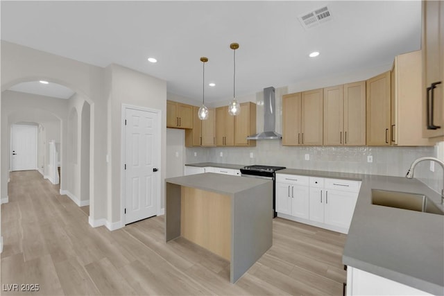 kitchen featuring arched walkways, stainless steel stove, visible vents, a sink, and wall chimney range hood