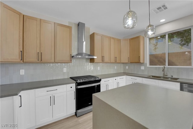 kitchen featuring stainless steel gas range oven, a sink, visible vents, backsplash, and wall chimney exhaust hood