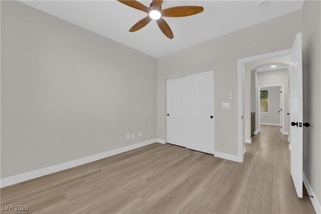 unfurnished bedroom with arched walkways, ceiling fan, light wood finished floors, and baseboards