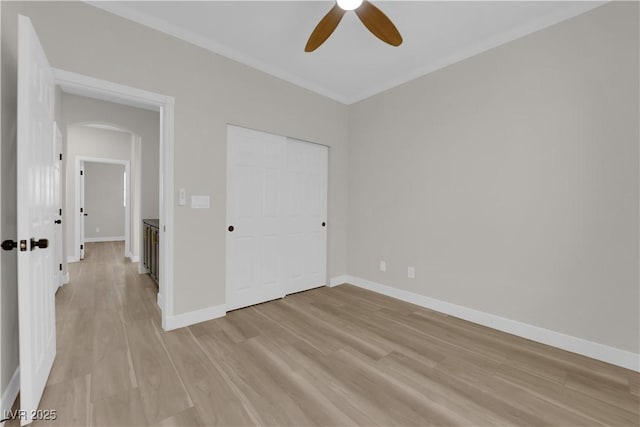 unfurnished bedroom featuring arched walkways, ceiling fan, light wood-style flooring, baseboards, and a closet