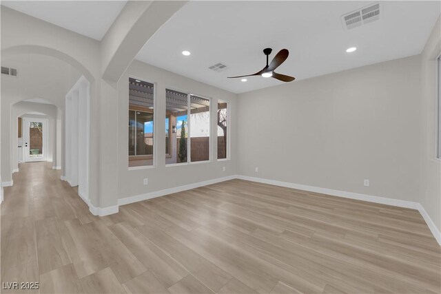 unfurnished room featuring light wood-style floors, arched walkways, visible vents, and baseboards