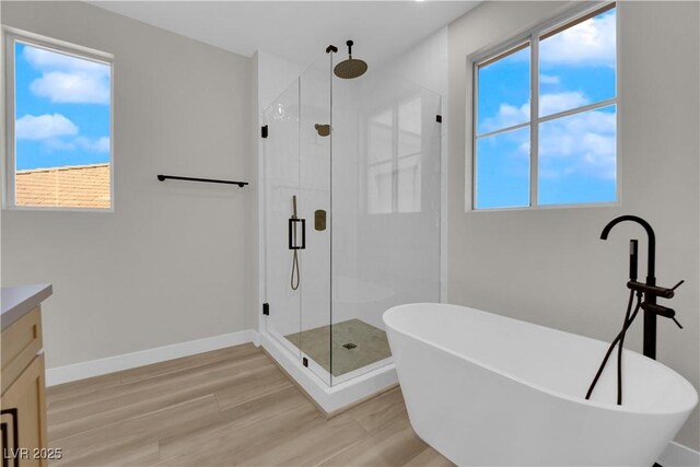 full bath with a freestanding tub, wood finished floors, vanity, baseboards, and a shower stall