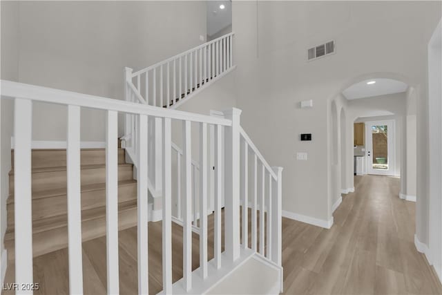 stairway with baseboards, visible vents, arched walkways, a towering ceiling, and wood finished floors