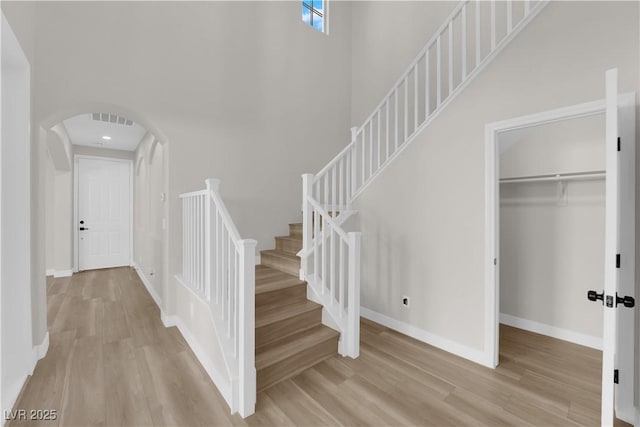 stairs with a towering ceiling, visible vents, arched walkways, and wood finished floors