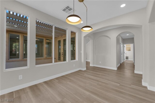 unfurnished room with light wood-style floors, arched walkways, visible vents, and baseboards