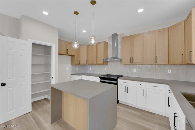 kitchen with light wood-style floors, wall chimney exhaust hood, stainless steel range with gas stovetop, and light brown cabinetry