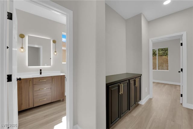 corridor with light wood-style floors, baseboards, and a sink