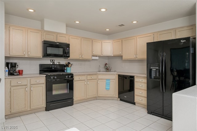 kitchen featuring light countertops, visible vents, light brown cabinetry, a sink, and black appliances