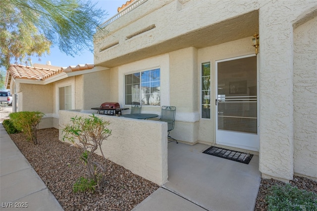 entrance to property with a tiled roof, a patio area, and stucco siding