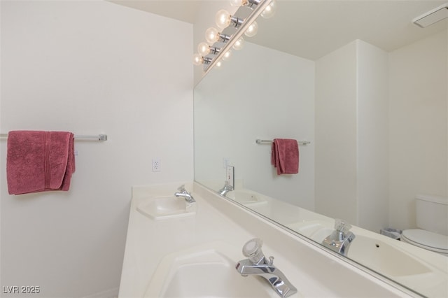 bathroom featuring visible vents, double vanity, a sink, and toilet