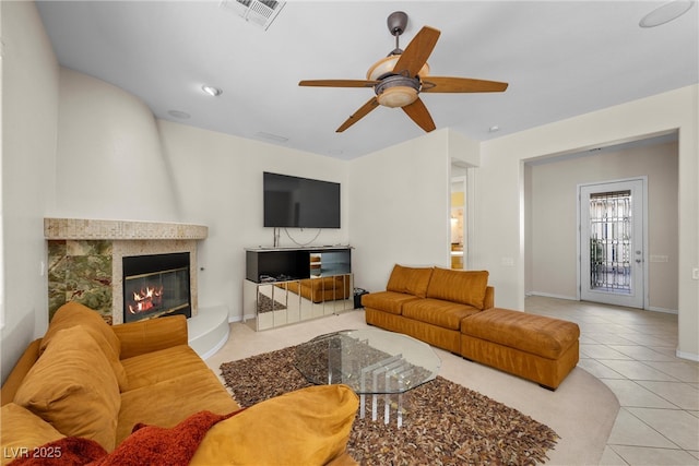 tiled living area featuring a ceiling fan, a tile fireplace, visible vents, and baseboards