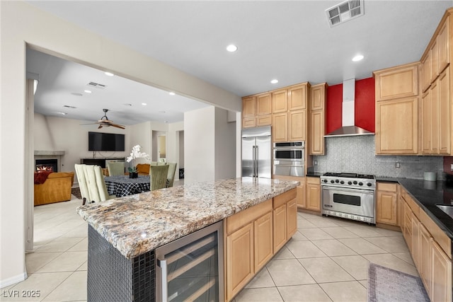 kitchen with decorative backsplash, wine cooler, high quality appliances, wall chimney range hood, and a fireplace