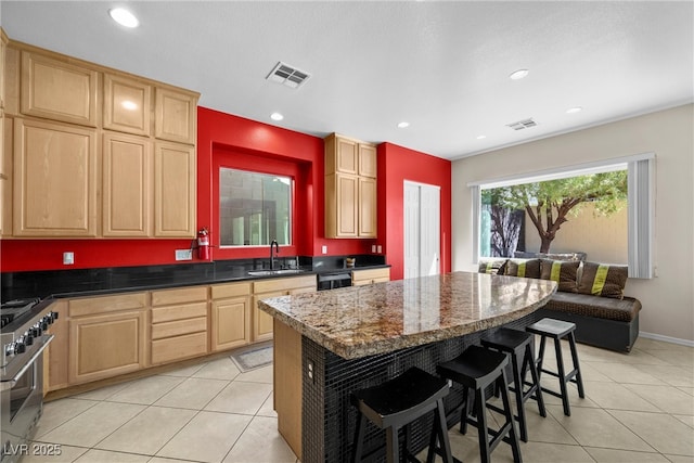 kitchen featuring stainless steel stove, visible vents, a sink, and light brown cabinetry