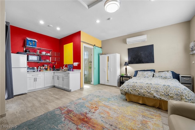 bedroom featuring light wood finished floors, a barn door, freestanding refrigerator, an AC wall unit, and a sink