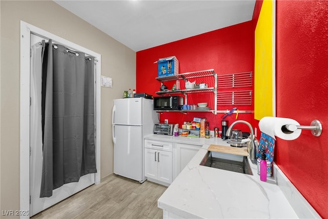 kitchen with black microwave, a sink, freestanding refrigerator, open shelves, and light wood finished floors