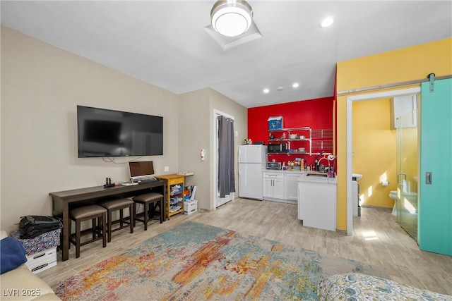 kitchen featuring a barn door, freestanding refrigerator, white cabinets, a sink, and light wood-type flooring